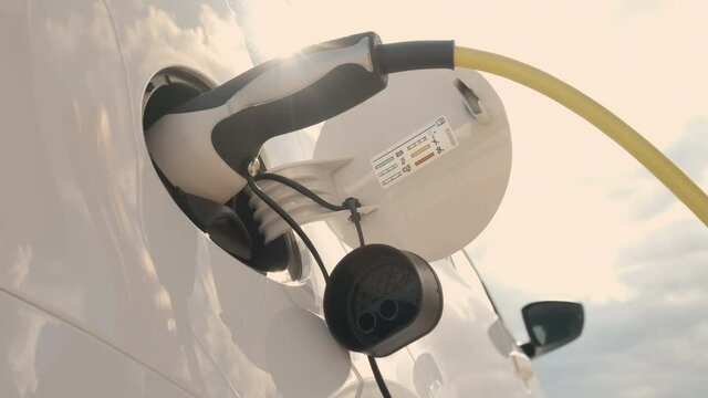 Bottom view of woman hand inserts power cable supply to charge electric or EV car on the background of blue sky