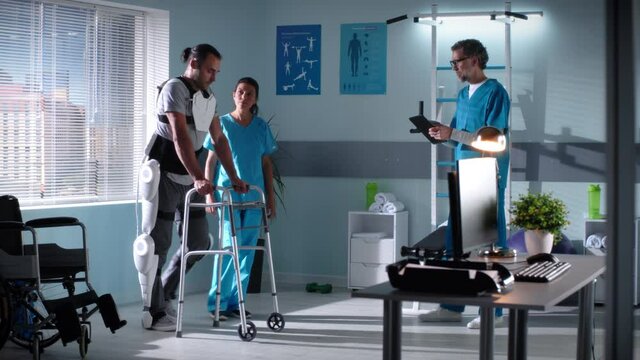 Man with exoskeleton and walking frame having rehabilitation session with doctors