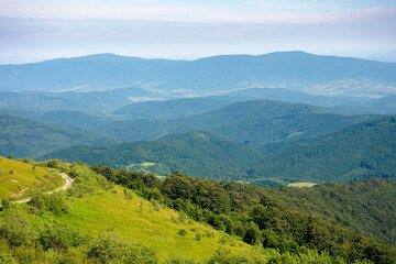 Naklejka premium country road through the hill. mountain landscape in morning light. blue sky with clouds on a horizon above the distant ridge. rural valley between the rolling hills in the distance