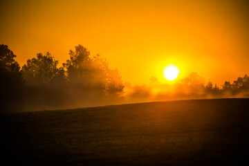 A sun disc shining through the mist during the summer sunrise. Summertime scenery of Northern Europe.