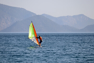 Windsurfing in the sea, water sports. View to windsurfer and green mountains in mist