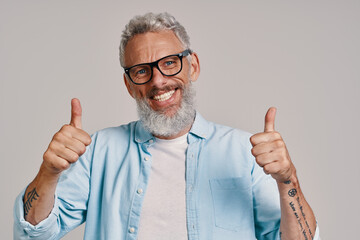 Handsome senior man in eyeglasses keeping thumbs up and smiling