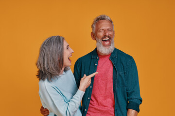 Obraz premium Beautiful senior couple laughing while standing together against orange background