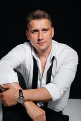 A stylish young man in a white shirt is sitting on the director's chair on a black background. A handsome charismatic businessman.
