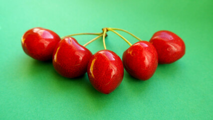 five red cherries lie side by side on a green background. front view