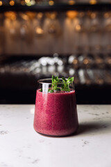 A glass of cold forest fruit berry smoothie cocktail garnished with a mint sprig, marble table.