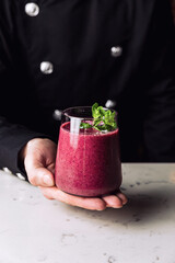 Bartender holding a glass of refreshing forest fruit berry smoothie cocktail garnished with a mint sprig, marble table.