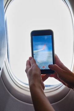 Woman takes pictures on the phone from the airplane window. Hand with a telephone near the porthole. Airplane wing, scenic view. Beautiful cloud, blue sky. Travel by plane, adventure. Air Transport