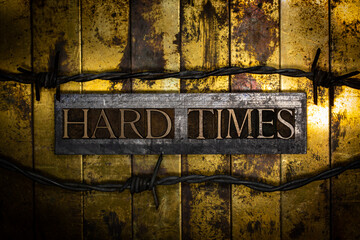 Hard Times text message lined with barbed wire on vintage textured grunge copper and gold background 