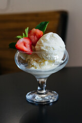 three white balls of ice cream in a glass cup or a bowl, a glass. Red strawberries cut in two with green petals as an ice cream decoration