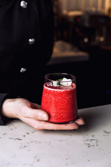 Bartender holding a glass of refreshing strawberry and banana smoothie cocktail garnished with an edible flower, marble table.