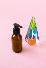 Close-up bottle with pump for beauty product mockup and glass pyramid prism on pink background with...