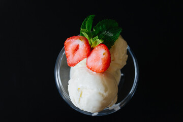 three white balls of ice cream in a glass cup or a bowl, a glass. Red strawberries cut in two with green petals as an ice cream decoration