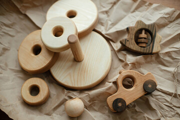 Eco friendly plastic free toys for toddler. Modern natural wooden pyramid with rings, teether hedgehog and car on craft paper on wooden table, top view. Stylish simple wooden toys for child