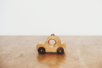 Fototapeta premium Road trip and travel concept. Stylish natural wooden car toy on table on white wall background. Space for text. Eco friendly plastic free toy for toddler. Stylish simple toy for child