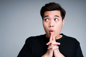 Scared and surprised asian guy puts his fingers to his mouth and looks to the side raising his...