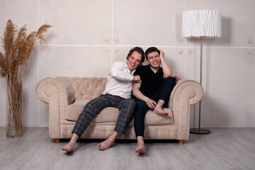 Naklejka premium Two handsome and lovely men are sitting on the couch. Best friends and leisure time together. Watching serials in front of the TV.