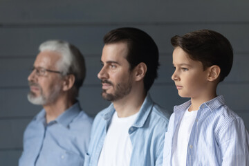 Serious boy, his father and grandpa standing together in row, looking forward. Portrait of three...