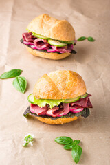 Ready-to-eat hamburgers with pastrami, cucumber, radish and herb on craft paper. American fast food. Vertical view