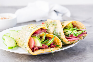 Egg rolls filled with pastrami, cucumber, radish and green onions on a plate on the table. Hearty and high-calorie snack