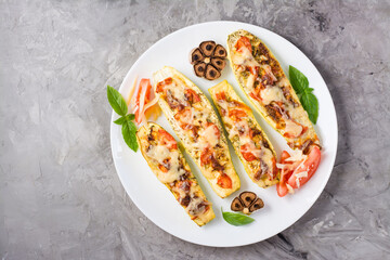 Ready-to-eat baked zucchini halves stuffed with cheese and tomato and basil leaves on a plate on the table. Vegetable dishes, healthy food. Top view. Copy space