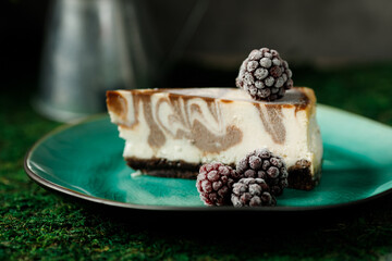Cheesecake with chocolate flavor is on a plate with blackberries.
