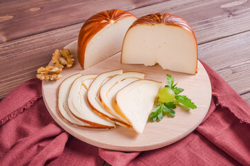 Cheese slices for menu, sausage cheese on a round board on a dark wooden background