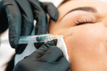 Plastic syrgery. Close-up of female face getting injection in the cosmetology salon. Doctor in medical gloves with syringe injects cheek a botulinum toxin