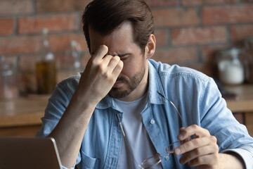 Sad business man, remote employee tired of work at computer, touching eyelids, closed irritable dry...
