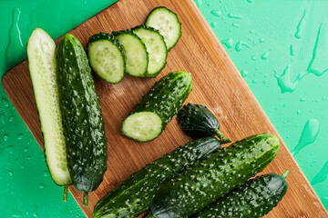 Set of fresh whole and sliced cucumbers on a wooden board with water drops. Garden cucumber wallpaper backdrop design