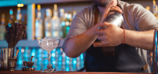 Closeup hand of bartender shaking cocktail ingredients in shaker on bar counter at nightclub
