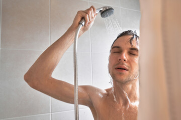 Portrait of young handsome man washes himself with shower gel, lathers head with shampoo in the...