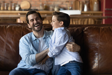 Joyful excited dad and son having fun at home, enjoying playtime on couch. Happy loving daddy...