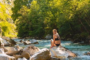 Fototapeta na wymiar smiling and happy young woman looking at camera sitting near a river in the forest. Rio Cares in Picos de Europa.