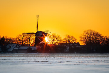 Frosty Dutch windmill, Sunrise in the village with Dutch windmill, orange sky, white snow field foreground, silhouette picture