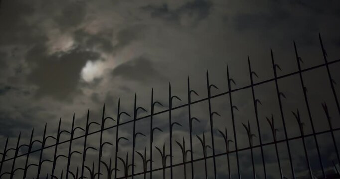 Time-lapse Clouds passing moon at night time. Full moon with cloudy night, spooky feeling like thriller horror films Halloween ghost mystery scary fairyland scene, focus at spike fence