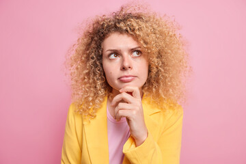 Portrait of good looking thoughtful woman ponders on decision keeps hand on chin looks away makes...