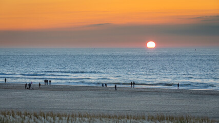 Sunset on the beach, Orange sky blue water silhouets on the strand shore sand
