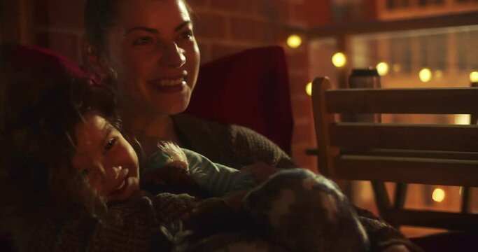 Mother and toddler girl on highrise condo patio at night.