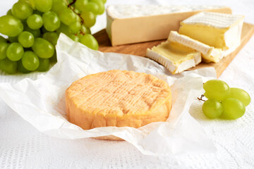 Delicious cheese brie or camembert on cutting board with bunch of grape on the table with white tablecloth. Dairy products. Italian, French cheese. Breakfast. Selective focus