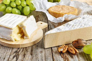 Delicious cheese brie or camembert on cutting board with bunch of grape on the table with white tablecloth. Dairy products. Italian, French cheese. Breakfast. Selective focus