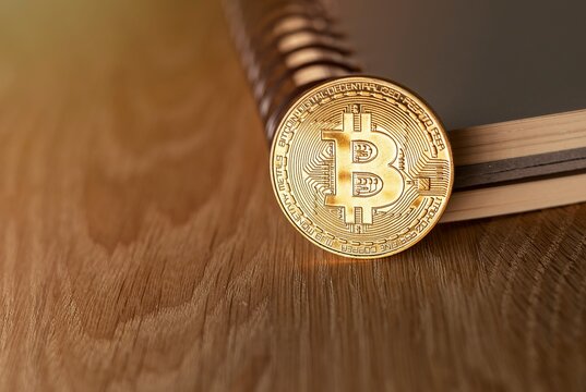 Golden shiny bitcoin coin on wooden desk, closeup.