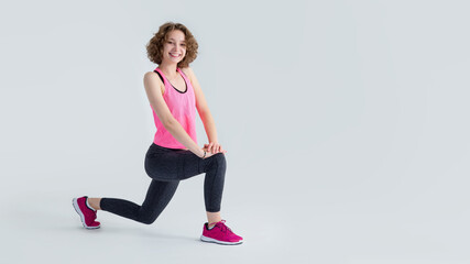 Sporty young woman doing leg stretch before fitness. Photo in the studio on a gray background.