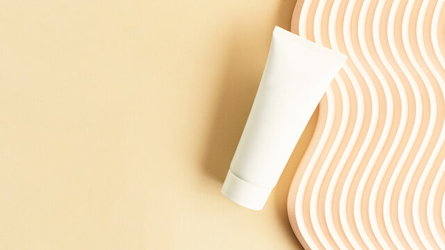 Blank white cosmetics tube on the beige background.Wavy podium near it.Good as cosmetic mockup,pastel large banner with copy space.