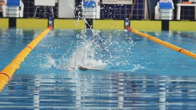 teenage swimmer swims in a free style in the pool at a swimming competition. The athlete has a dark cap on his head. He is approaching the finish line. Close-up, slow motion.