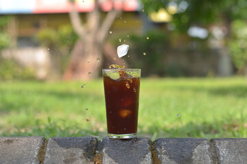 ice cube falling to Iced Coffee in the glass refreshing look with blurred background. selective focus