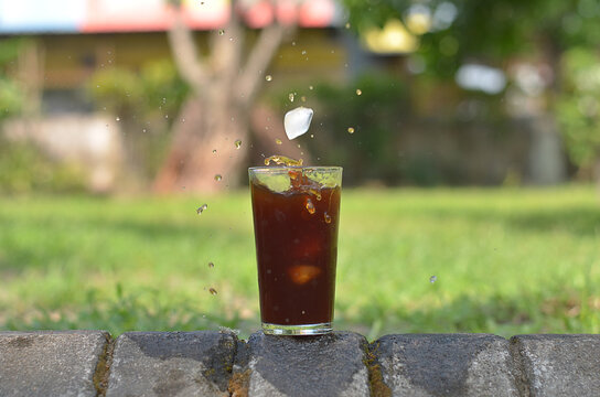 ice cube falling to Iced Coffee in the glass refreshing look with blurred background. selective focus