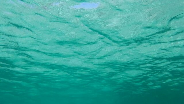 Slow motion, surface of green water. Natural background with sun glints on surface of the water. Texture of gren water surface of sea reflection of sun's rays. Underwater shot