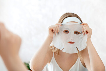 Woman apply Mask sheet on face. Facial skincare cloth mask. Teenage girl do beauty face care therapy. Home beauty spa treatments. Daily hygiene Self Care morning daily routine
