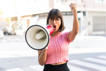 Young brunette woman in the city shouting through a megaphone to announce something